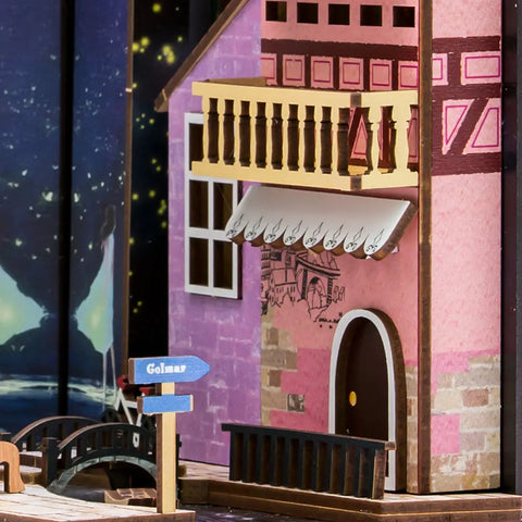 Une maison de poupée miniature colorée avec un balcon et un auvent.