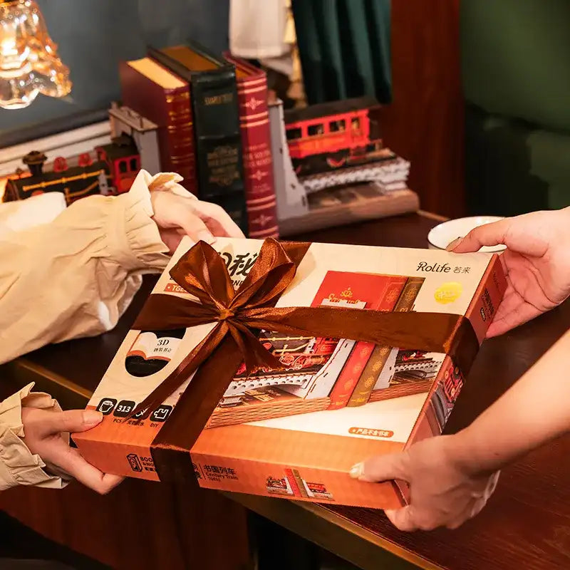 Un coffret cadeau noué avec un ruban brun, contenant des maquettes miniatures ou des livres représentant des scènes de train.