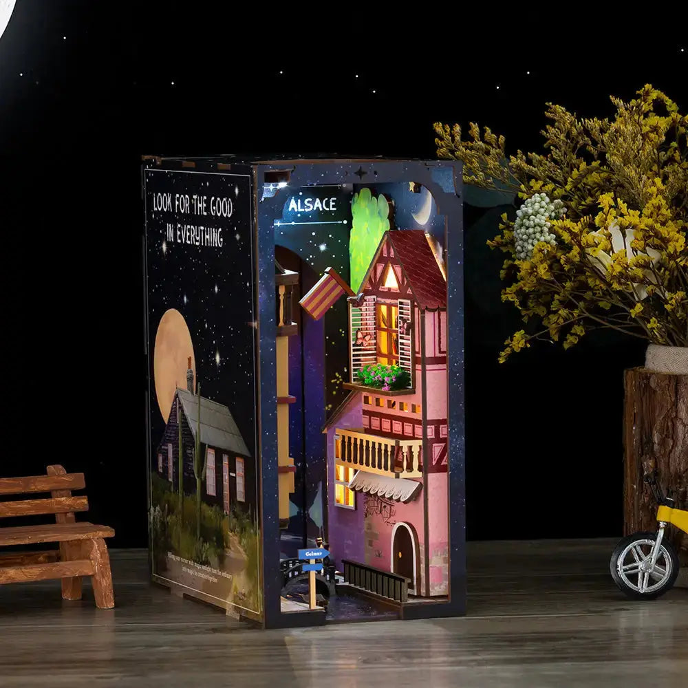 Diorama miniature illuminé dans un insert de bibliothèque, représentant une charmante scène de rue européenne avec des maisons détaillées et un ciel nocturne.