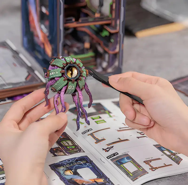 Modèle miniature d’une créature violette à tentacules avec un œil central, assemblé à l’aide d’une pince à épiler.