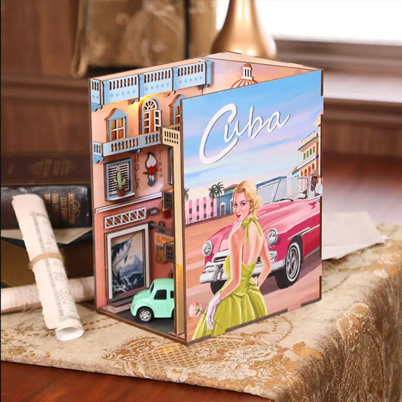 Diorama miniature en bois d’une scène de rue cubaine avec une voiture classique et une femme.