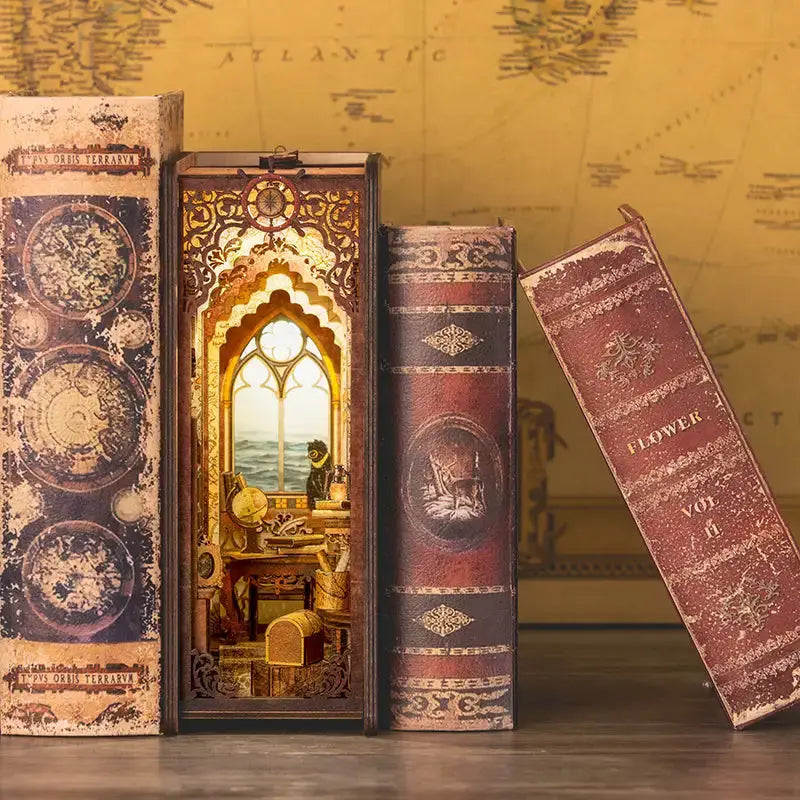 Un coin livre décoratif avec un diorama éclairé d’un bureau surplombant une mer agitée, flanqué de deux faux livres anciens et d’un livre penché.