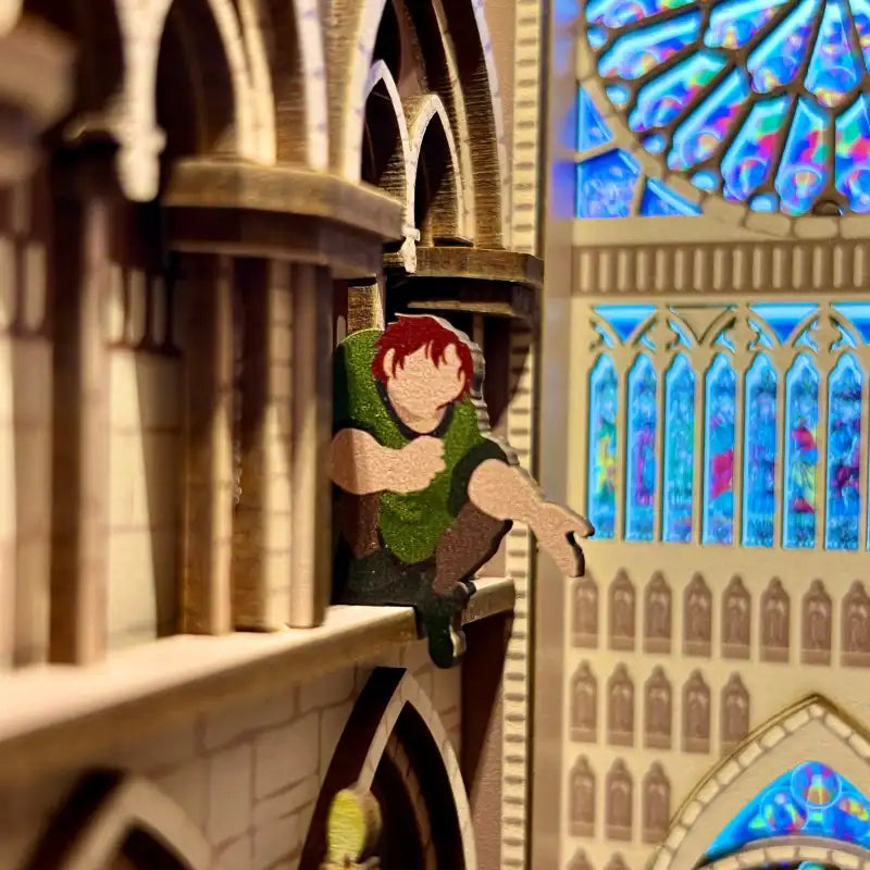 Un découpage en bois de Quasimodo du ’Bossu de Notre-Dame’ de Disney perché sur un bâtiment miniature.