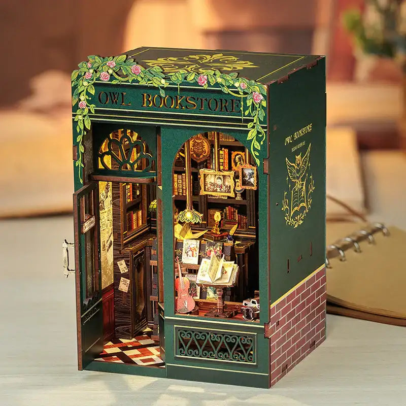 Un diorama miniature détaillé d’une librairie pittoresque et illuminée avec une porte ouverte et un intérieur complexe.