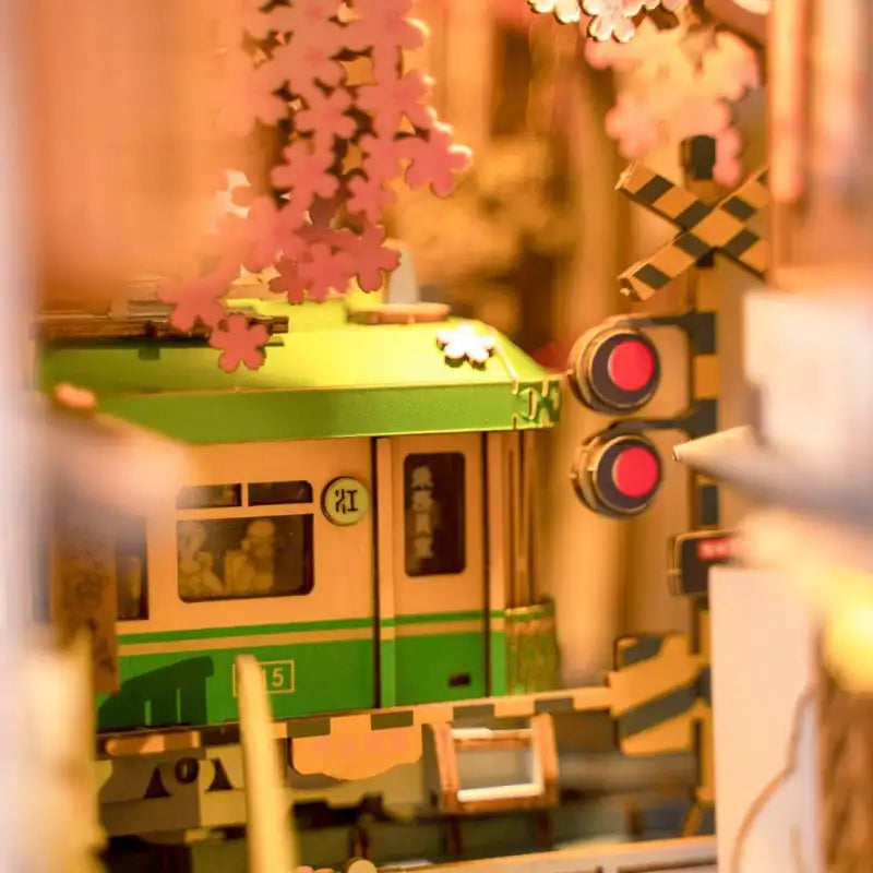 Train miniature en bois avec un toit vert et une carrosserie beige, avec des fenêtres et des fleurs de cerisier décoratives.