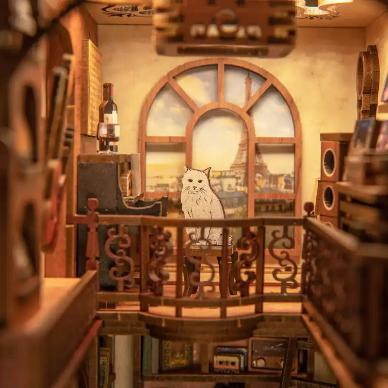 Diorama miniature d’une scène d’intérieur avec un chat découpé, une fenêtre donnant sur la Tour Eiffel et divers petits meubles.