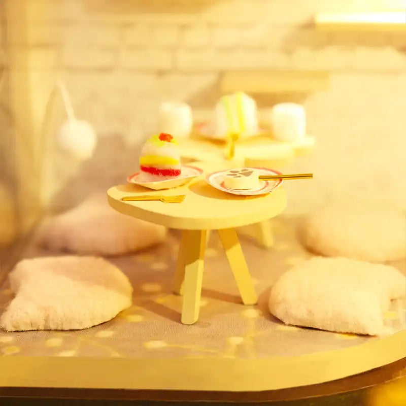 Une table de dessert miniature avec des gâteaux, des assiettes et des coussins.