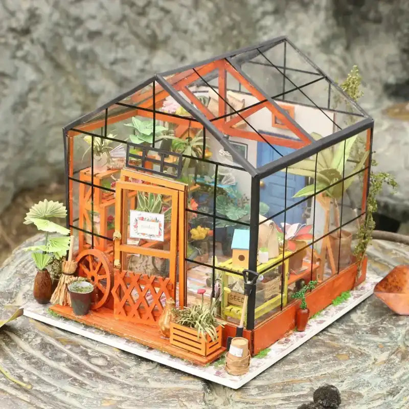 Un modèle miniature de serre bricolée, très détaillé, avec diverses plantes et accessoires de jardinage à l’intérieur.