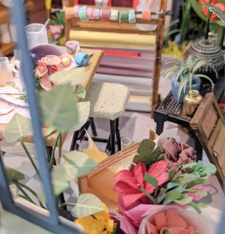 Une salle de bricolage miniature avec des bouquets de fleurs en papier et des rouleaux de ruban.