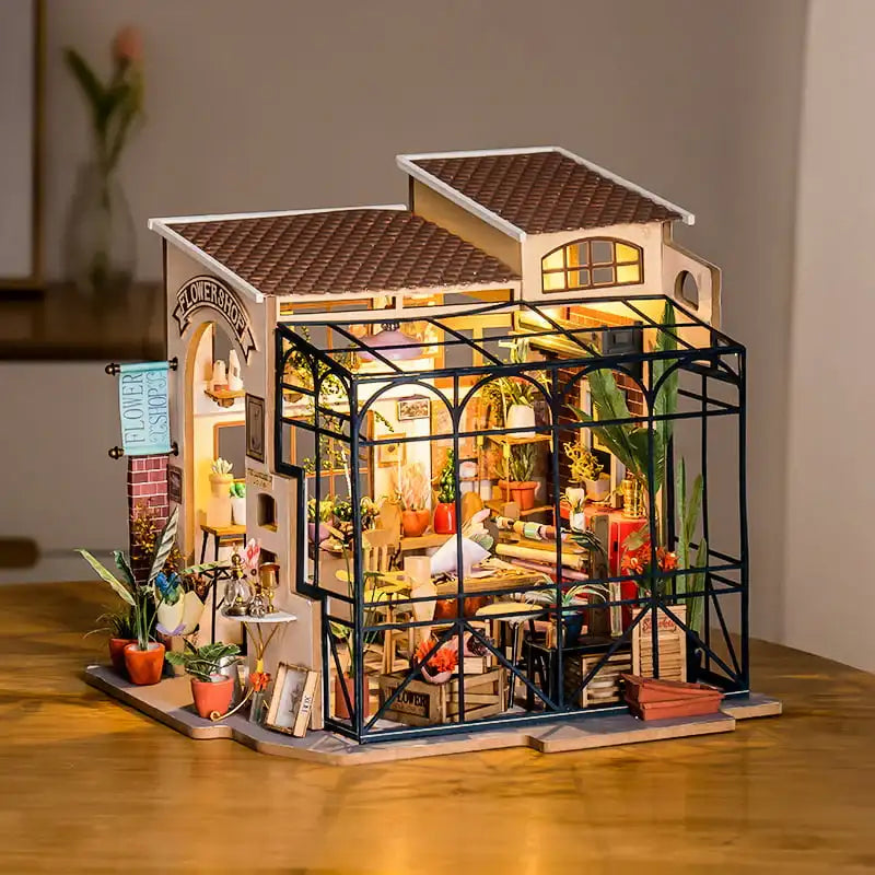 Un magasin de fleurs miniature éclairé avec une serre dans une maison de poupée.