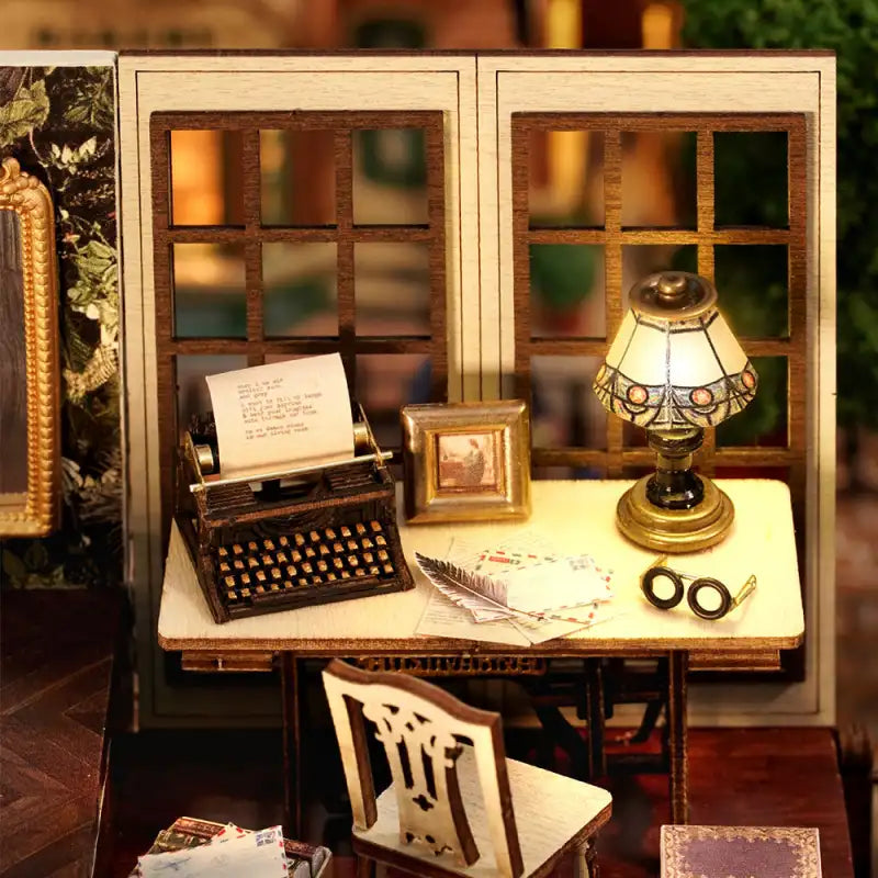 Bureau de poupée miniature avec une machine à écrire vintage, une lampe à vitrail et un tableau encadré sur un bureau.