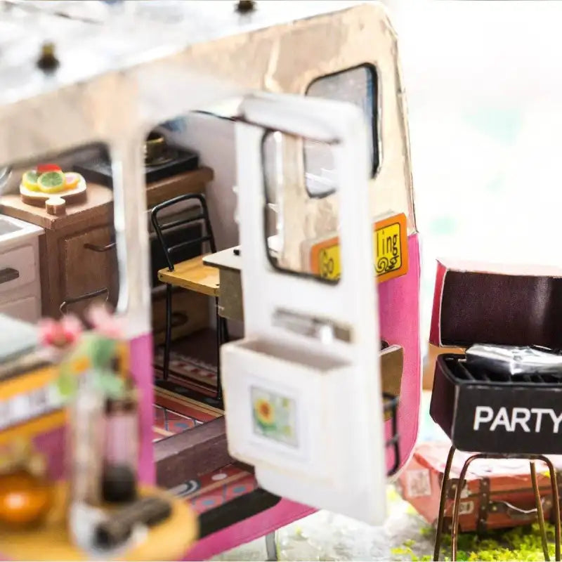 Camping-car miniature dont la porte ouverte laisse apparaître un intérieur avec des meubles.