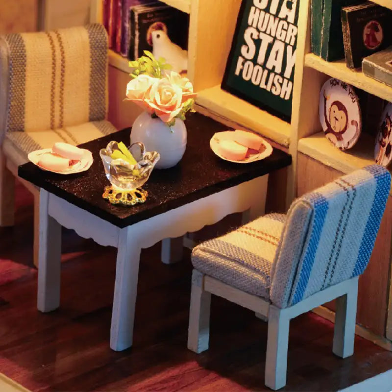 Ensemble de salle à manger miniature pour deux personnes, composé d’une table noire et de deux chaises rembourrées.