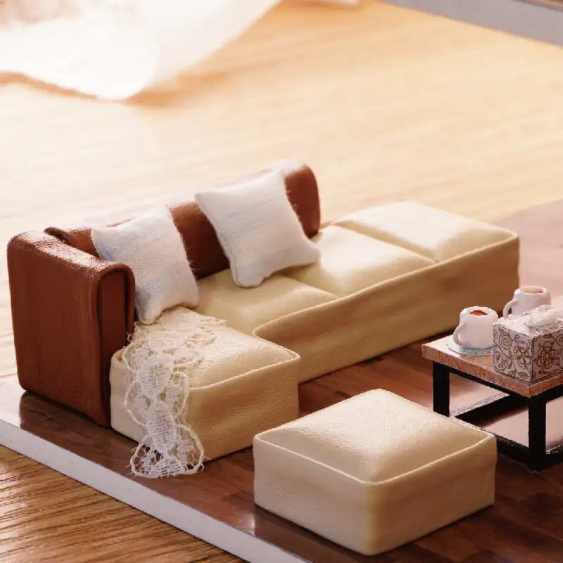 Canapé sectionnel miniature en forme de L avec un ottoman, avec un revêtement marron et crème et des coussins blancs.