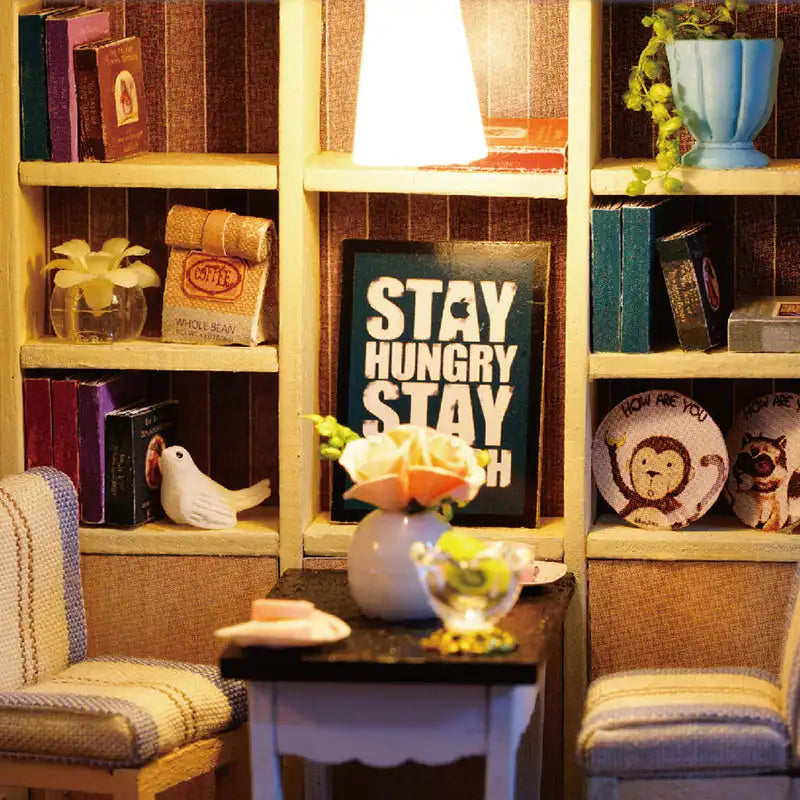 Une étagère miniature remplie de livres et d’objets décoratifs, avec une petite table et des chaises au premier plan.