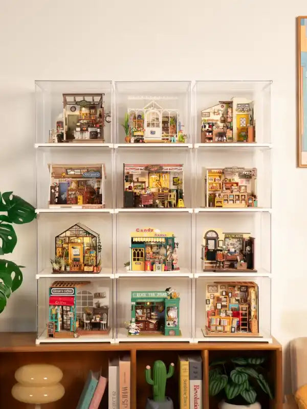 Une collection de douze vitrines miniatures de maisons de poupées présentées dans des boîtiers individuels en acrylique transparent.