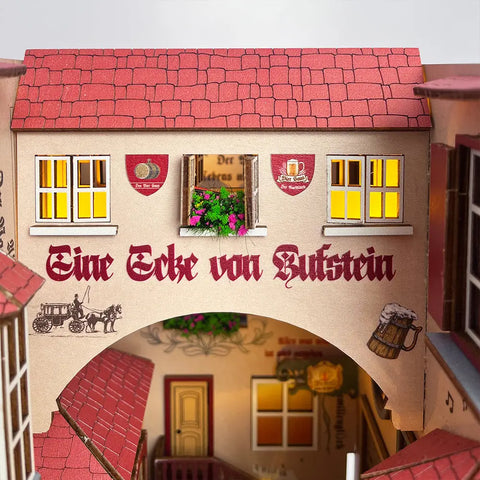 Un modèle miniature détaillé d’un bâtiment en bois avec un toit rouge, des fenêtres éclairées et un texte en allemand.