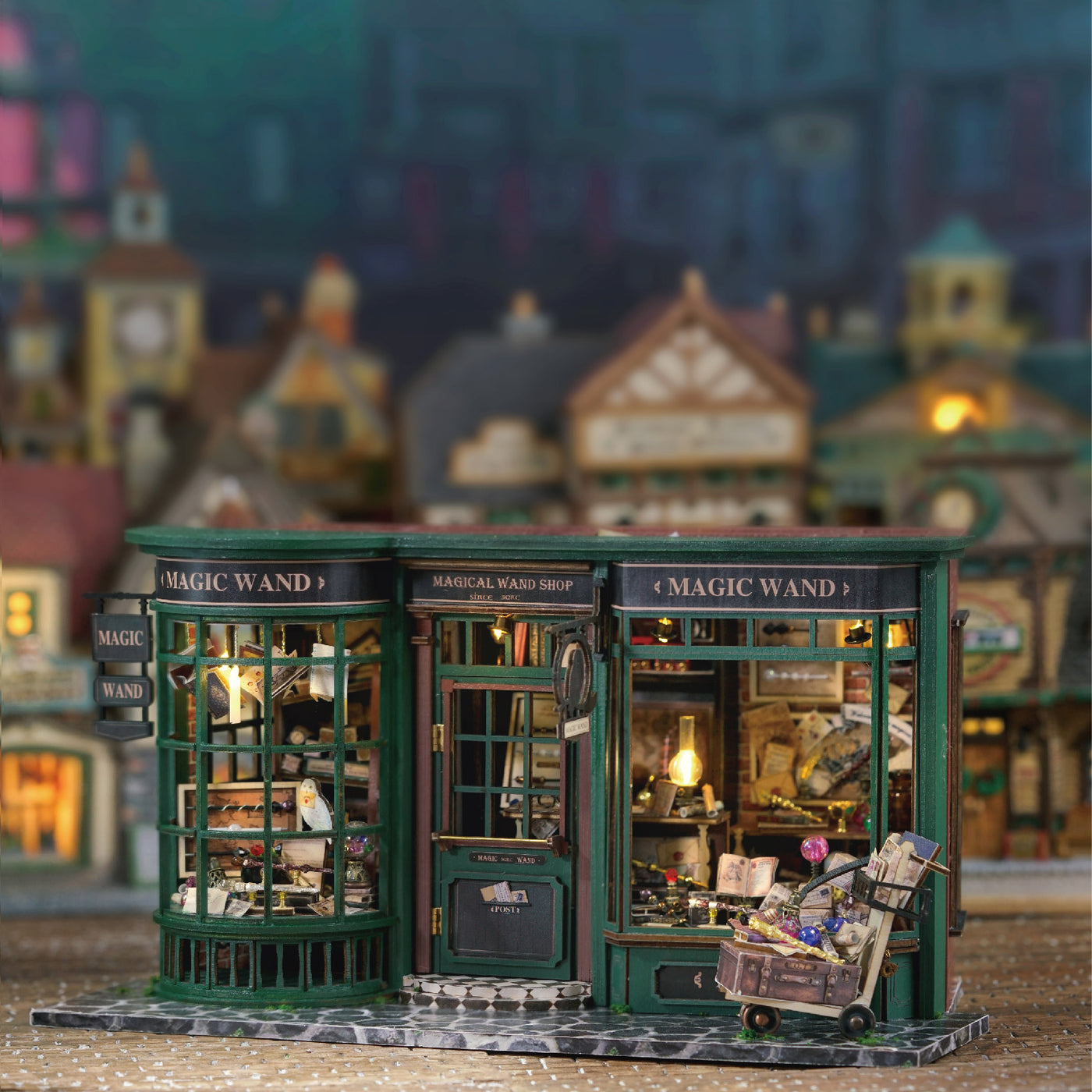 Un magasin de baguettes magiques miniature, illuminé, vert foncé, avec des vitrines détaillées et un chariot débordant de marchandises.