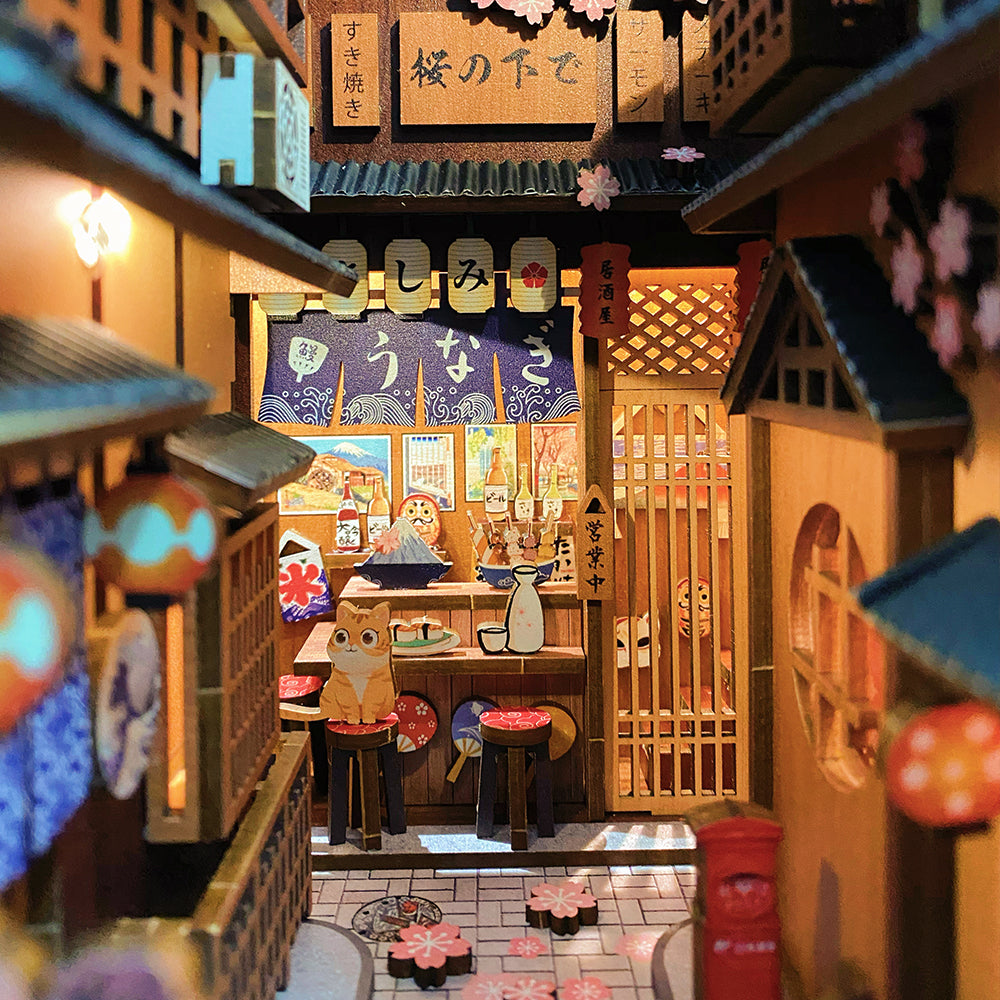 Une scène de rue japonaise miniature avec un izakaya et des cerisiers en fleurs.