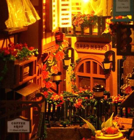 Scène de rue miniature dans une maison de poupée avec un éclairage vibrant et des décorations florales.