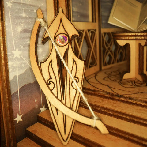 Un arc et un bouclier miniatures en bois avec un bijou irisé.